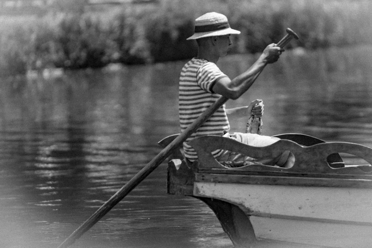 Man rowing a small boat with one oar while holding a bottle